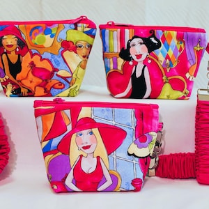 May include: Three fabric pouches with zipper closures, each featuring colorful illustrations of stylized figures. Two pouches include detachable, gathered pink wrist straps with silver-toned hardware. The designs incorporate vibrant shades of pink, yellow, and blue.