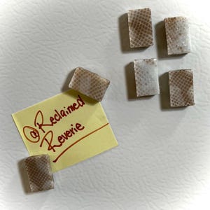 Op de afbeelding: Verschillende rechthoekige stukken met een slangenleerpatroon, sommige met een gespikkelde witte uitstraling. Een gele plakbriefje met de tekst "@Reclaimed Reverie" is ook zichtbaar.