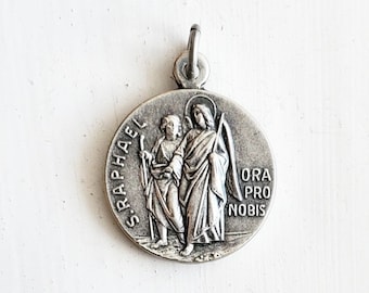May include: Silver pendant featuring a depiction of the archangel Raphael with a staff and a young man. The pendant is inscribed with "S. Raphael" and "Ora Pro Nobis".
