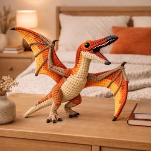 May include: A crocheted Pterodactyl dinosaur in shades of orange, tan, and brown, with open wings. The handmade creature has a detailed head, open mouth, and black claws. It is posed on a wooden surface, with a blurred background of a bedroom.