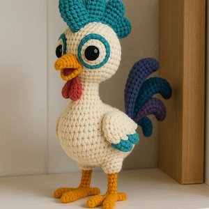 Puede incluir: Una figura de pollo tejida a ganchillo con cuerpo color crema, una cresta de color verde azulado brillante y grandes ojos negros con anillos del mismo tono. Tiene un pico amarillo, una barbilla roja, patas naranjas y una cola azul oscuro.