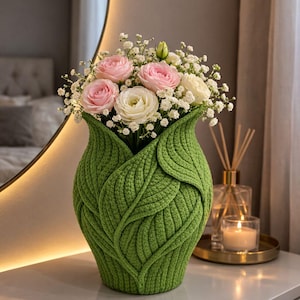 May include: A white ceramic mug with a black handle and the text "But First, Coffee" in a bold, black font. The mug is set against a blurred background, suggesting a cozy setting.