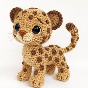 May include: A crocheted leopard cub with a tan body and dark brown spots. The handmade toy has large black eyes, a tan muzzle, and small whiskers. The ears and tail tip are dark brown. The cub is standing on all fours.