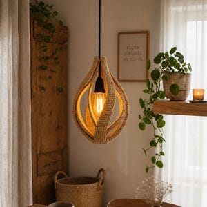 May include: A beige crochet pendant light fixture with a teardrop shape hangs from a black cord. The light bulb is visible inside the fixture. The room has a wooden cabinet, a basket, and a framed picture on the wall.