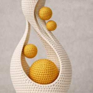 May include: A cream-colored, crocheted vase with a teardrop shape, holding four golden-yellow spheres of varying sizes. The vase has a textured surface and a modern, artistic design, suitable for home decor.