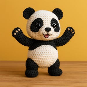 May include: A handmade crochet panda bear with a black and white color scheme. The panda has black eyes, ears, arms, and legs, with a white face, belly, and body. The panda is standing with its arms raised, and a smiling expression.