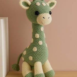 May include: A handmade crochet giraffe toy in shades of green and cream. The giraffe has a long neck, small horns, and is adorned with white polka dots. The toy is sitting on a wooden shelf, with a neutral background.