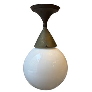 Op de afbeelding: Een vintage plafondlamp met een witte globe kap. De armatuur heeft een messingkleurige kegel en een donkerbruine, gestileerde, gebogen bovenkant. Het licht is ontworpen om aan het plafond te worden gemonteerd.
