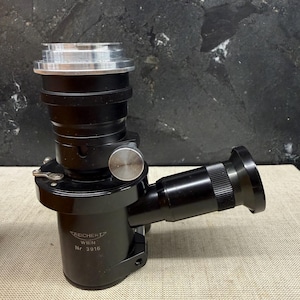 May include: A black and silver vintage microscope with a cylindrical body and an angled eyepiece. The microscope has a silver top and a black base with the text "Reichert Wien Nr 3916".