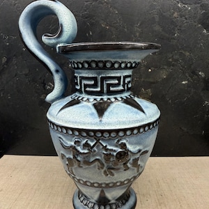 Könnte beinhalten: Eine blaue Keramikvase mit einem großen, gebogenen Henkel. Die Vase hat schwarze geometrische Muster und einen Fries mit Figuren auf Pferden. Die Vase ist etwa 30 cm hoch.