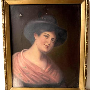 Könnte beinhalten: Ein antikes Porträtgemälde in einem goldenen Rahmen. Das Kunstwerk zeigt eine Frau mit schwarzem Hut und rosa Schal. Das Gemälde hat einen dunklen Hintergrund und ist in einem dekorativen Goldrahmen gerahmt, was seinen Vintage-Charme unterstreicht.