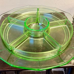 Könnte beinhalten: Ein Vintage-Serviertablett aus hellgrünem Glas mit geteiltem Design. Das Tablett hat einen zentralen kreisförmigen Bereich und vier Kuchenförmige Fächer, alle in einer größeren, achteckigen Form. Das Glas hat einen leichten Glanz.