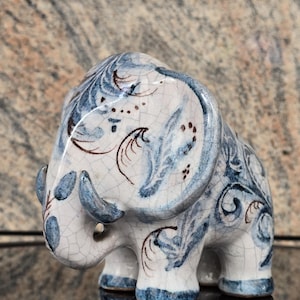 Könnte beinhalten: Eine Keramik-Elefantenfigur mit weißem Sockel und blau-braunen Dekorationsmustern. Der Elefant hat ein detailliertes Design an Ohren, Rüssel und Körper. Die Figur ist ein dekoratives Objekt.