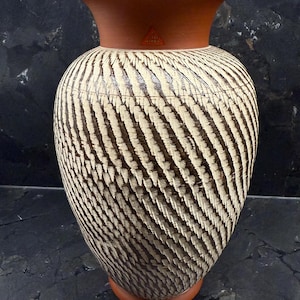 Könnte beinhalten: Eine dekorative Keramikvase mit breitem, rundem Körper und ausgestelltem Rand. Die Vase hat ein strukturiertes Muster aus diagonalen cremefarbenen und braunen Streifen. Der Rand und der Sockel sind terrakottafarben. Die Vase ist ca. 30 cm hoch.