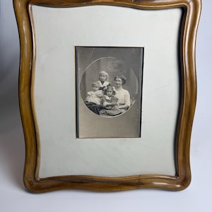 Könnte beinhalten: Ein antiker Holzbilderrahmen mit einem Foto einer Frau und drei Kindern. Der Rahmen hat ein hellbraunes, geschwungenes Design. Das Foto ist kreisförmig und wird von einem weißen Passepartout umgeben.