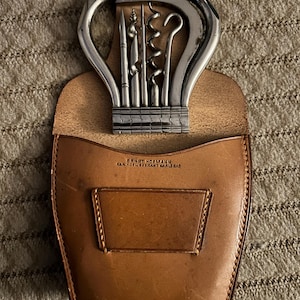 Può includere: Un set di apribottiglie vintage con un apribottiglie in metallo argentato e vari strumenti, tra cui un cavatappi, in una custodia di pelle marrone. La custodia è impressa con il testo "ERNST HOFMANN" e altro testo.