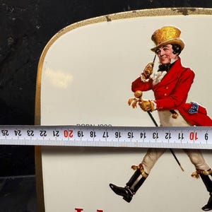 Puede incluir: Letrero met&aacute;lico rectangular vintage con borde dorado. El letrero presenta el logotipo de Johnnie Walker Striding Man en rojo y blanco, con el texto "Johnnie Walker" en la parte inferior. El letrero mide aproximadamente 23 cm de ancho.