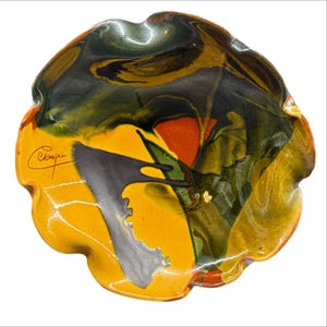 Puede incluir: Un cuenco decorativo de cerámica hecho a mano con una forma orgánica única. El cuenco presenta una vibrante paleta de colores amarillo, naranja, verde y negro, con un acabado brillante. La firma del artista es visible en el lateral.