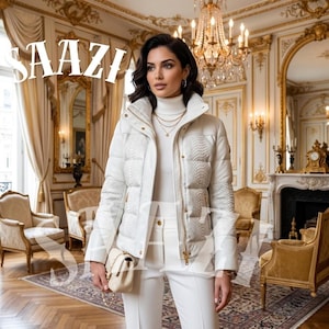 Può includere: Una donna indossa una giacca trapuntata bianca con un motivo strutturato sulle maniche e sulle spalle, abbinata a pantaloni bianchi e una borsa coordinata. La giacca ha un collo alto e dettagli dorati. La parola "SAAZI" è visualizzata in bianco.