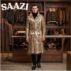 May include: A long trench coat with a tan and black snakeskin pattern, featuring a wide collar, a matching belted waist, and long sleeves. The text SAAZI is visible at the top left and centre of the image. The coat is worn over a black turtleneck.