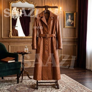 Peut inclure: Un long trench-coat marron clair avec un motif texturé façon autruche, un col à revers, des manches longues avec poignets et une ceinture assortie dotée d'une boucle rectangulaire. Le manteau est boutonné sur le devant et suspendu.