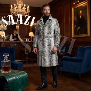 Puede incluir: Un abrigo tipo trench de doble botonadura con estampado de piel de serpiente y cinturón. El abrigo es gris y blanco, y el modelo lleva un cuello alto negro, pantalones negros y zapatos negros. La palabra "SAAZI" está en texto blanco.
