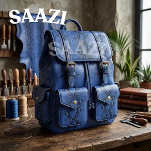 Könnte beinhalten: Ein blauer Rucksack mit schwarzem Schlangenledermuster, ausgestattet mit einem Tragegriff, einer Klappe mit zwei Schnallenriemen, einem Kordelzugverschluss und zwei Vordertaschen mit Druckknöpfen. Das Wort SAAZI ist auf und über der Tasche gedruckt.