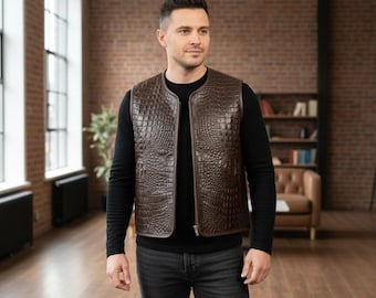 Può includere: Un gilet marrone con texture a pelle di coccodrillo. Il gilet ha una chiusura a zip ed è indossato sopra una maglia nera a maniche lunghe. La persona indossa jeans neri.