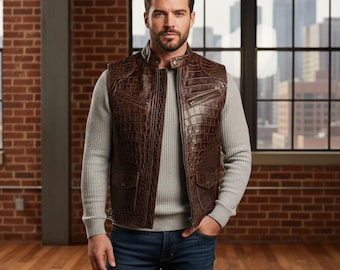 Può includere: Un gilet in pelle marrone con motivo a pelle di coccodrillo. Il gilet ha una chiusura con cerniera, tasche e un colletto rialzato. La persona indossa un maglione grigio e jeans blu.
