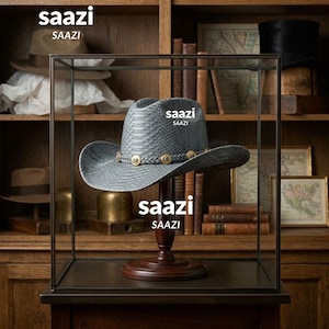 May include: A grey cowboy hat with a snakeskin-like texture and a braided hatband featuring metallic circular studs. The hat is displayed on a dark wooden stand inside a glass case. The text "saazi" is visible in multiple locations on the image.