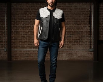 Può includere: Un gilet in pelle nera con spalle e tasche con motivo a pelle di serpente bianca. Il gilet ha una texture a coccodrillo sui pannelli anteriori e posteriori. La persona indossa una maglietta nera e jeans blu. Lo sfondo è un muro di mattoni.