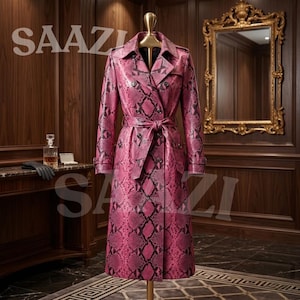 Peut inclure: Un trench-coat à double boutonnage avec un motif peau de serpent rose et noir, un col à revers, des manches longues avec des poignets à boucle et une ceinture à nouer assortie à la taille, présenté sur un mannequin dans une pièce lambrissée.