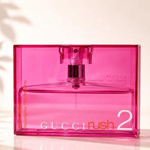 May include: A vibrant pink perfume bottle with a clear glass interior. The bottle features a silver atomizer and the words "GUCCI Rush 2" are printed in white. The words "Vaporisateur Natural Spray" are printed on the side.