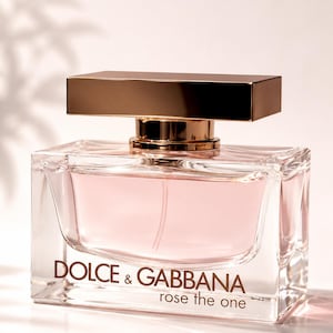 Könnte beinhalten: Rechteckiger Parfümflakon aus Glas mit rosa Flüssigkeit. Der Flakon hat einen goldfarbenen Deckel und trägt den Aufdruck "DOLCE & GABBANA rose the one" auf der Vorderseite.