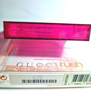 May include: A vibrant pink perfume bottle and box set. The box displays the brand name "Gucci Rush". The transparent bottle sits above the box, which has a barcode and other printed details.