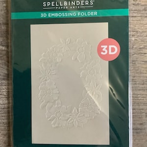 May include: A 3D embossing folder by Spellbinders Paper Arts. The package is dark green with a cream-colored cardstock inside. The cardstock features a floral wreath design. The folder measures 5.5 x 8.5 inches.