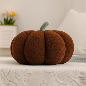 May include: A plush, brown pumpkin-shaped pillow with a green stem. The pillow has a textured, fuzzy surface and is designed to resemble a real pumpkin. Perfect for fall decor.