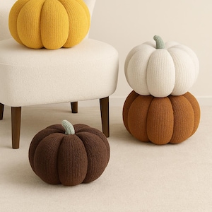 Puede incluir: Cojines decorativos con forma de calabaza en varios colores. Las calabazas están hechas de tela de punto y tienen un tallo de color contrastante. Hay una calabaza amarilla, otra blanca y otra marrón.