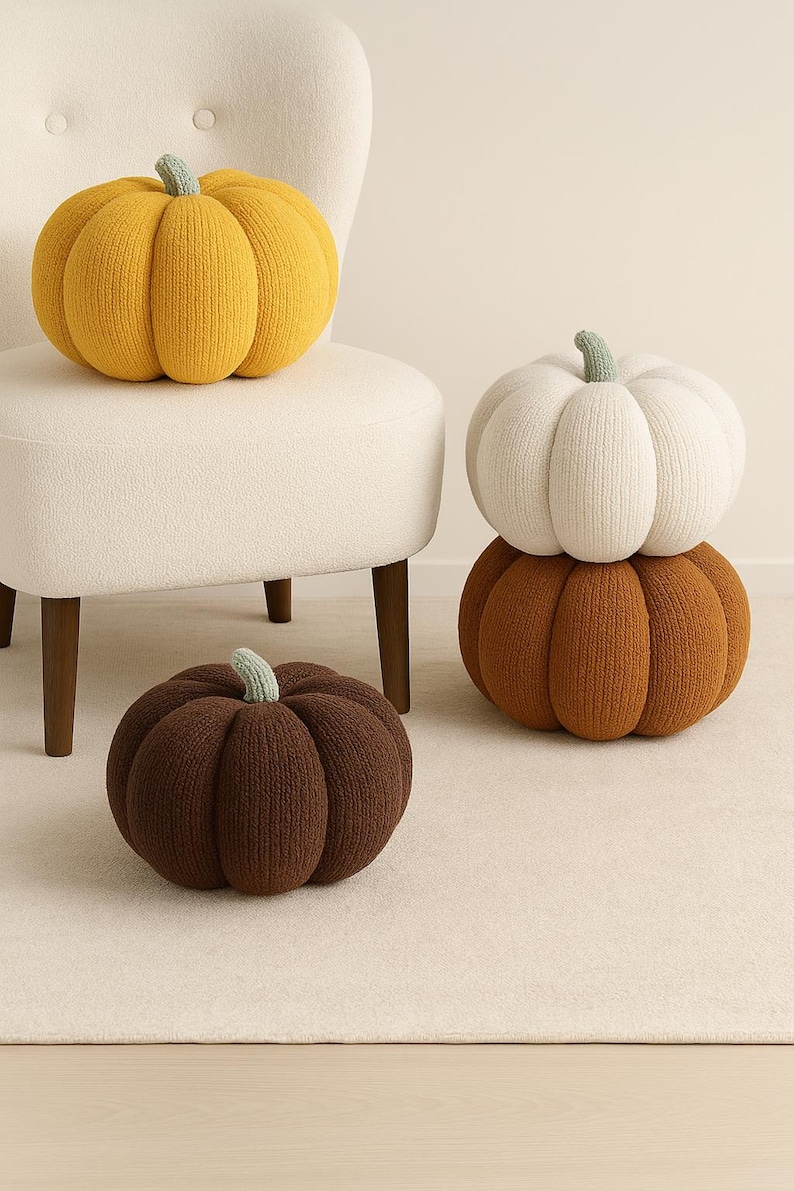 May include: A collection of decorative pumpkin-shaped pillows in various colors. The pumpkins are made of knitted fabric and feature a stem in a contrasting color. One pumpkin is yellow, another is white, and a third is brown.