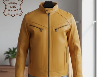 Könnte beinhalten: Eine senfgelbe Lederjacke mit Stehkragen und Druckknopf, durchgehendem Frontreißverschluss, zwei Brusttaschen mit Reißverschluss sowie zwei vertikalen Seitentaschen mit Reißverschluss. Ein Abzeichen trägt die Aufschrift GENUINE 100% LEATHER.