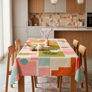 Puede incluir: Un mantel rectangular con borde festoneado que presenta un patrón geométrico de cuadrados, círculos y rectángulos en tonos rosa, verde oliva, azul claro y naranja. La tela cubre una mesa de comedor de madera con cuatro sillas.