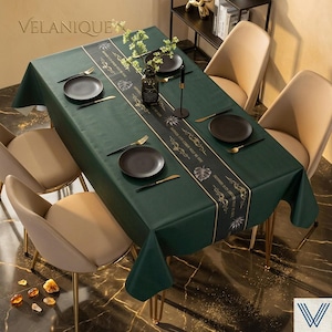 May include: A dark green rectangular tablecloth with a decorative black and gold center runner. The table is set with black plates, gold utensils, and a floral centerpiece. The brand name "VELANIQUE" is visible.