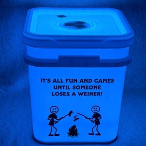 May include: A blue, square-shaped container with a matching lid. The container has the text "IT'S ALL FUN AND GAMES UNTIL SOMEONE LOSES A WEINER!" and features stick figures roasting food over a campfire. The container glows.