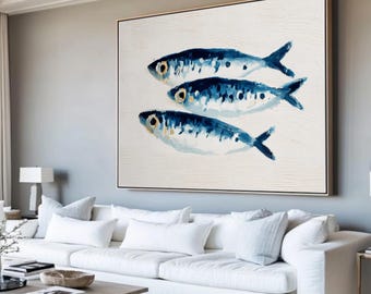 May include: A framed canvas art piece featuring three stylized blue fish painted on a white background. The fish have dark blue markings and yellow eyes. The artwork is displayed in a living room setting.