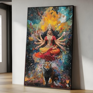 Op de afbeelding: Een ingelijst kunstwerk dat een veelarmige godheid in een zittende houding afbeeldt, gekleed in rode en gouden kleding, met een tijger eronder. De achtergrond heeft een levendig, kleurrijk abstract ontwerp met spetters blauw, geel en oranje.