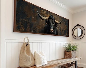 May include: A framed canvas art piece featuring a black bull with large horns. The artwork is set against a dark, textured background with brown and gold tones. The frame is a dark brown color. The artwork is displayed above a wooden bench in a hallway.