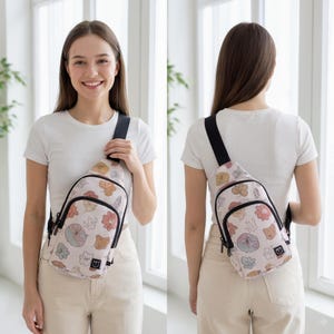 May include: A light pink sling bag with a black strap and zipper. The bag features a repeating pattern of colorful cartoon flowers and other shapes. The bag is worn over the shoulder.