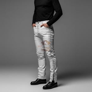 Puede incluir: Pantalones blancos con detalles de cordones negros en los laterales. Los pantalones, de corte ajustado, se combinan con zapatos negros y una camisa negra de manga larga. Un logotipo es visible cerca del bolsillo izquierdo.