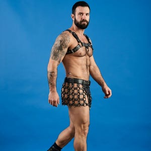 Könnte beinhalten: Ein schwarzer Brustgurt aus Leder mit verstellbaren Riemen und Metallschnallen, kombiniert mit einem passenden schwarzen Lederrock oder Kilt mit Gittermuster, der mit einem breiten Gürtel an der Taille befestigt wird und ein strukturiertes Design aufweist.