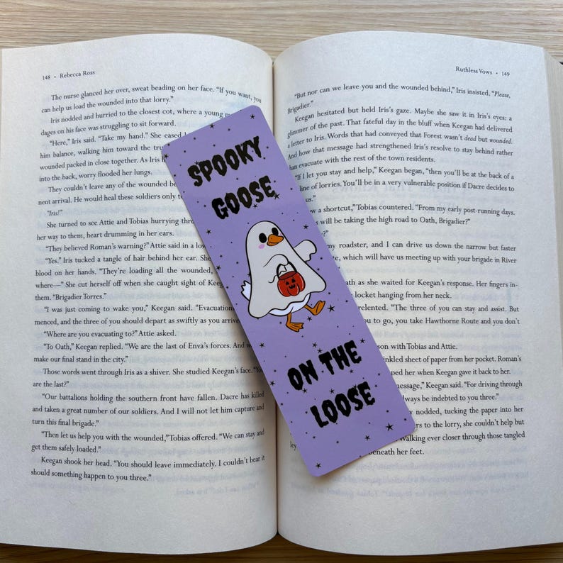 Purple bookmark with tiny black stars as the background with a goose dressed as a ghost with a candy bucket, with the words "spooky goose on the loose"